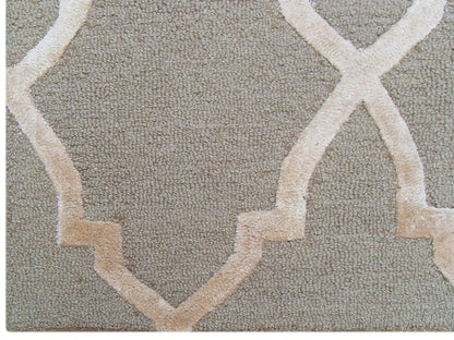 A close-up of the KOHINOOR MOCCA hand-tufted rug, featuring a soft, slightly raised beige trellis geometric pattern on a light brown background, reminiscent of Moroccan style.